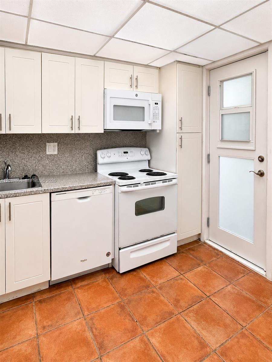 A kitchen features white cabinets, white appliances, a speckled countertop, and terracotta floor tiles — 240 Galen Dr # 214, Key Biscayne FL 33149, KEY BISCAYNE, FL