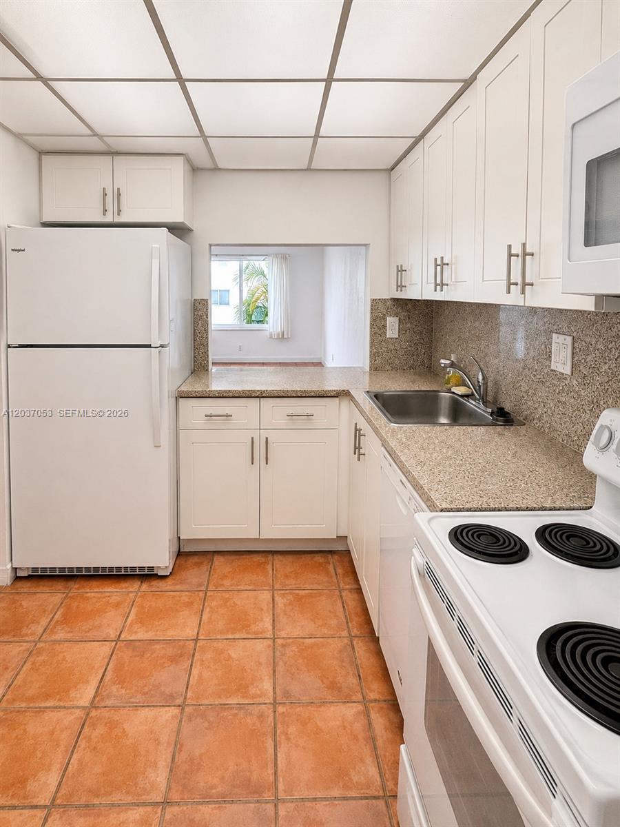A kitchen features white cabinets, granite countertops, a white refrigerator, and orange tile flooring — 240 Galen Dr # 214, Key Biscayne FL 33149, KEY BISCAYNE, FL