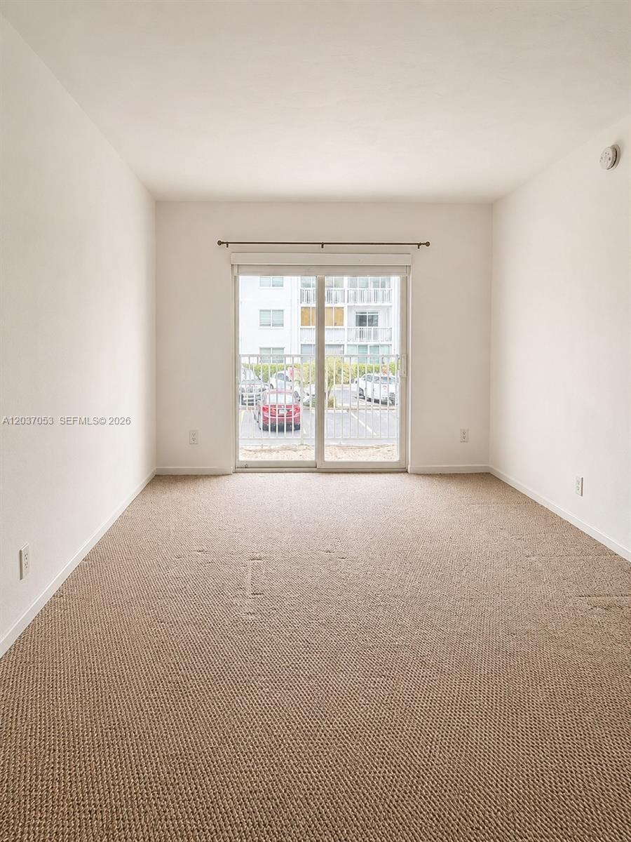 An empty room features beige carpeting, white walls, and a sliding glass door to a balcony — 240 Galen Dr # 214, Key Biscayne FL 33149, KEY BISCAYNE, FL