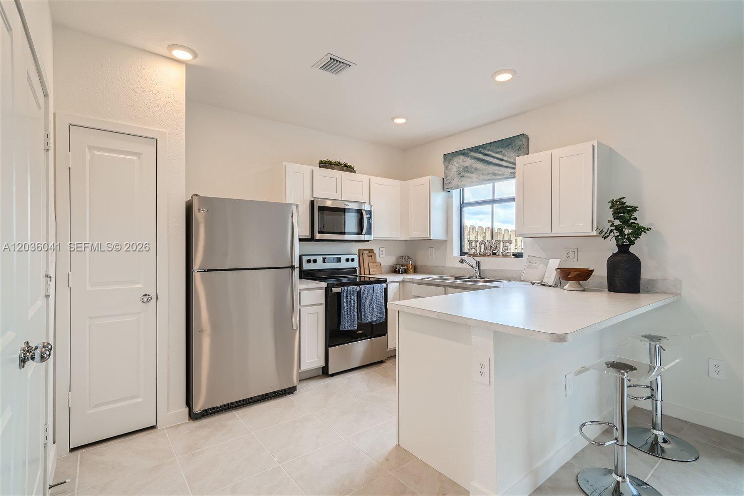 A kitchen features white cabinets, stainless steel appliances, and a breakfast bar with stools — 1366 NE 4th Ave, Florida City FL 33034, FLORIDA CITY, FL