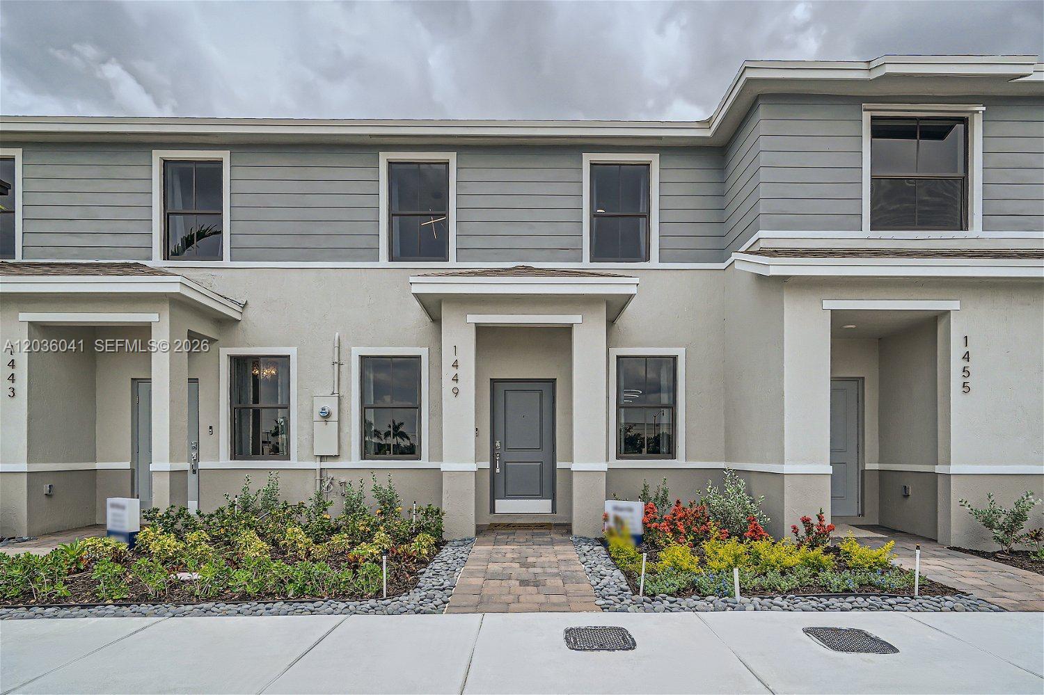 A two-story townhouse exterior features a gray front door, stone walkway, and landscaped garden beds — 1366 NE 4th Ave, Florida City FL 33034, FLORIDA CITY, FL