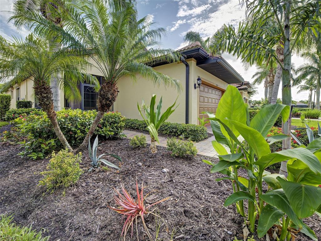 A landscaped front yard with palm trees and shrubs leads to a house with a garage — 13810 LIDO STREET, VENICE, FL