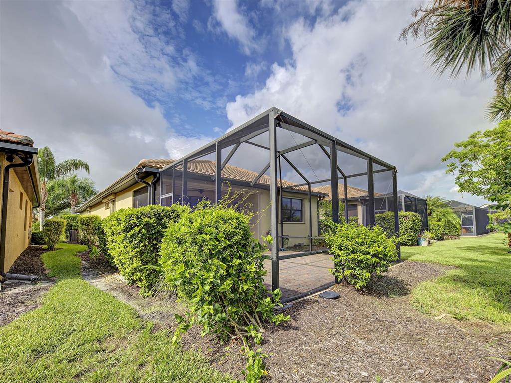 A backyard view of a house with a screened-in patio and surrounding landscaping — 13810 LIDO STREET, VENICE, FL