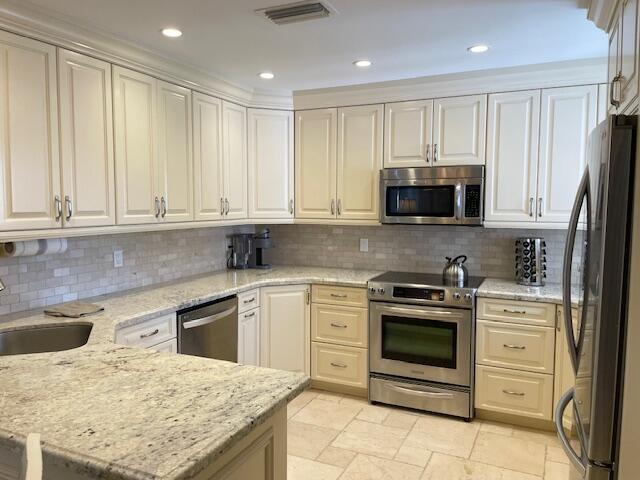 A kitchen with cream cabinets, granite countertops, stainless steel appliances, and light tile flooring — 2502 N Fairway Dr Drive N, Jupiter FL 33477, JUPITER, FL
