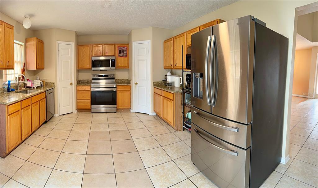 A kitchen with oak cabinets, granite countertops, stainless steel appliances, and light-colored tile flooring — 510 LOBELIA DRIVE, DAVENPORT, FL