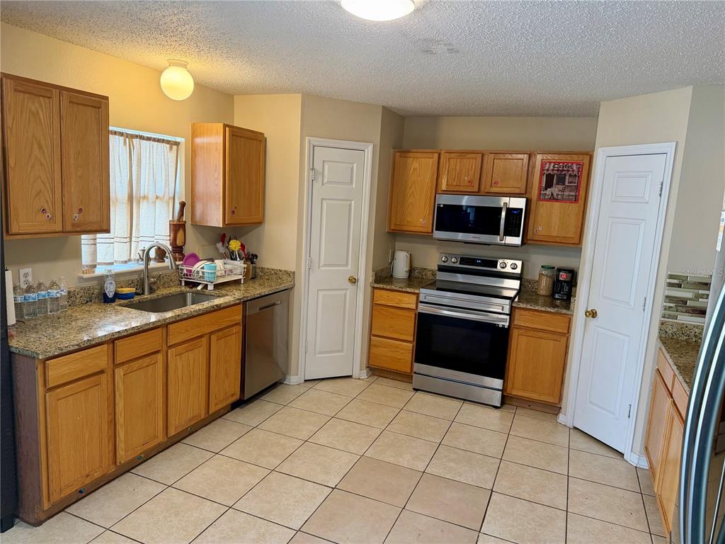 A kitchen with oak cabinets, granite countertops, stainless steel appliances, and beige tile flooring — 510 LOBELIA DRIVE, DAVENPORT, FL