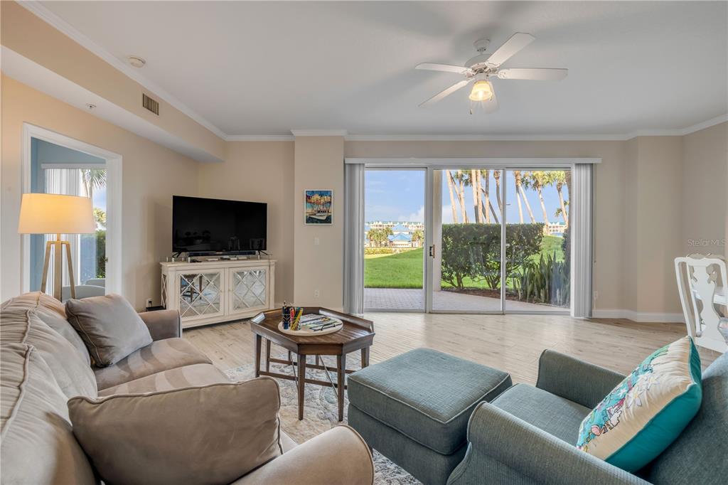 A living room features a beige sofa, blue armchair, television console, and sliding glass doors — 4650 LINKS VILLAGE DRIVE UNIT B103, PONCE INLET, FL