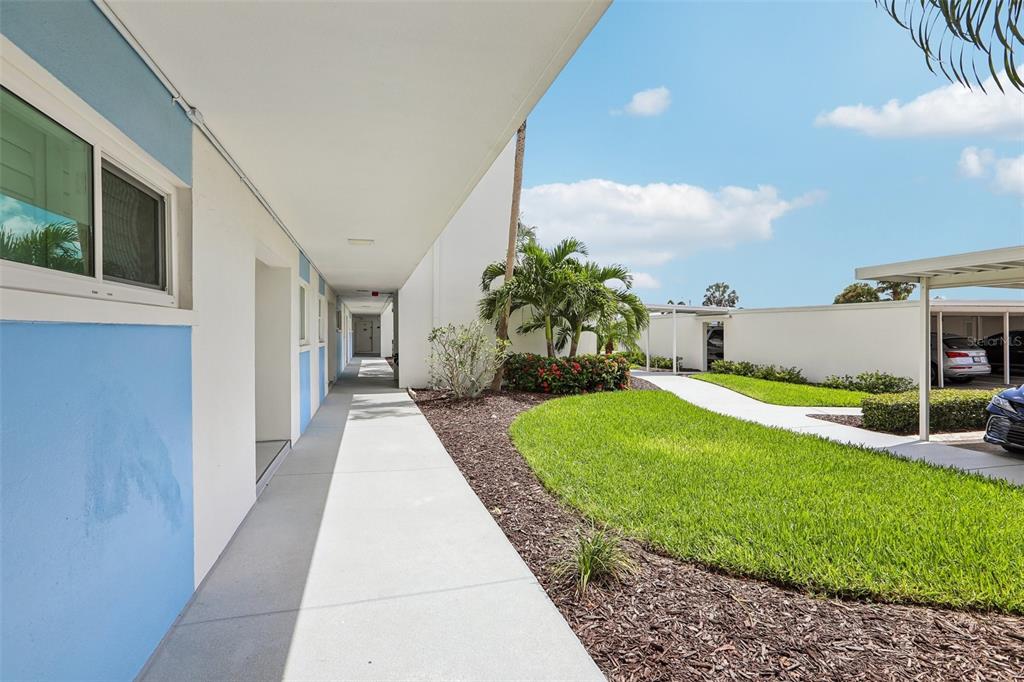 An outdoor walkway leads past a blue and white building toward a landscaped courtyard — 770 ISLAND WAY UNIT N204, CLEARWATER, FL