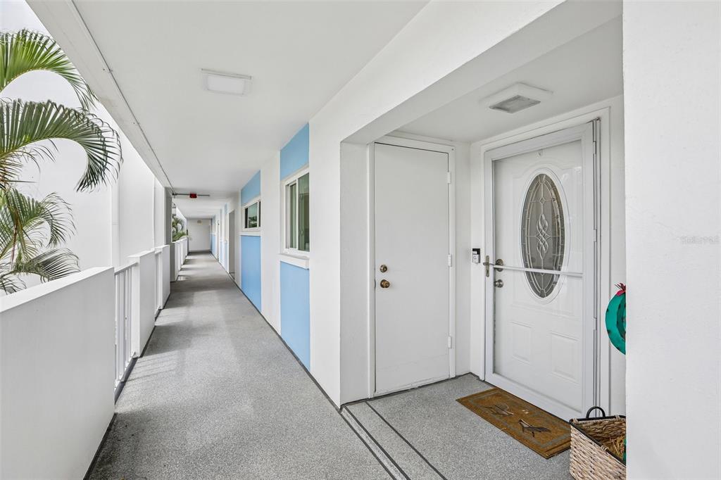 An outdoor apartment hallway features white walls with blue accents, a white door, and flooring — 770 ISLAND WAY UNIT N204, CLEARWATER, FL