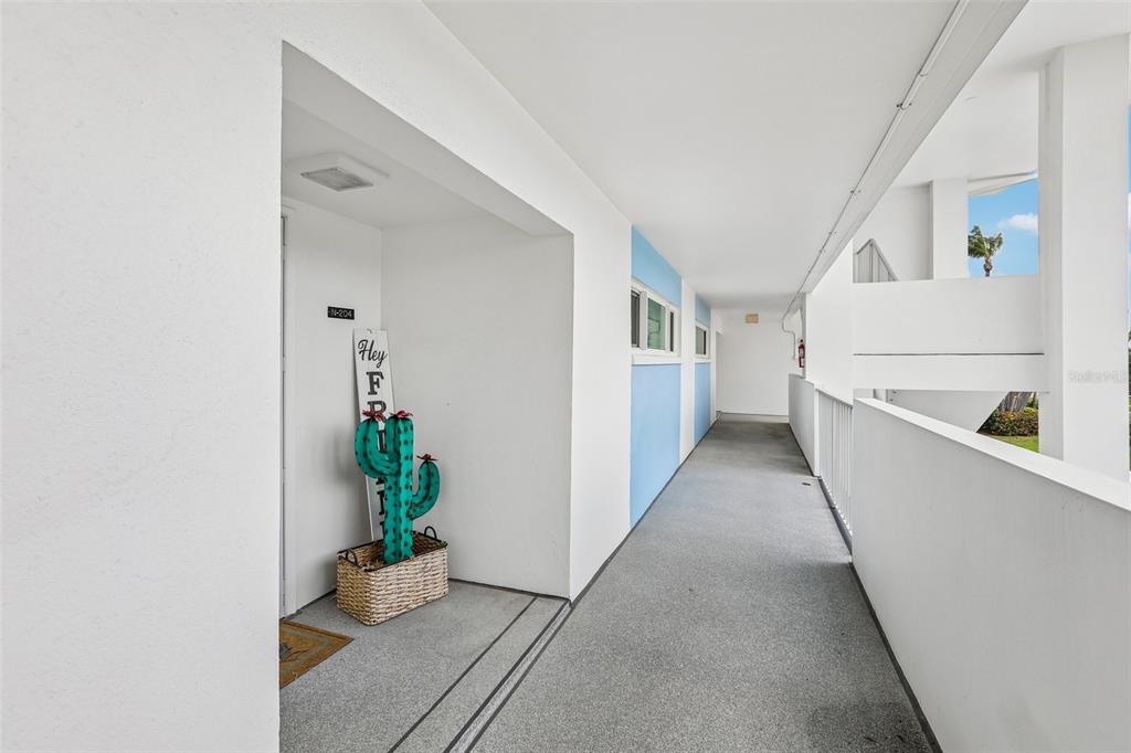 An outdoor apartment hallway features white walls, blue accents, and a decorative cactus door sign — 770 ISLAND WAY UNIT N204, CLEARWATER, FL
