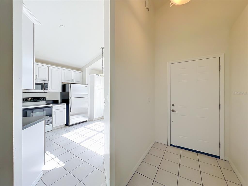 A view from a tiled entryway looking into a kitchen with white cabinets and appliances — 554 WHITTINGHAM PLACE, LAKE MARY, FL