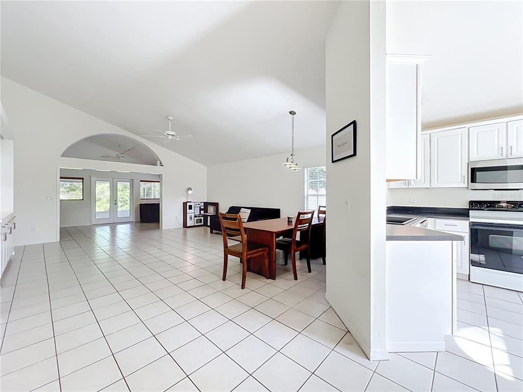 A bright, open-concept living and dining area features white tile flooring and a vaulted ceiling — 554 WHITTINGHAM PLACE, LAKE MARY, FL