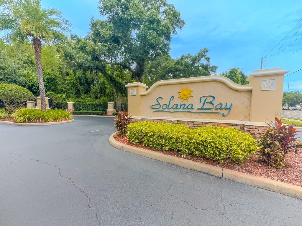 A beige community entrance sign for Solana Bay sits beside a paved road and landscaping — 8505 SANDY BEACH STREET, TAMPA, FL