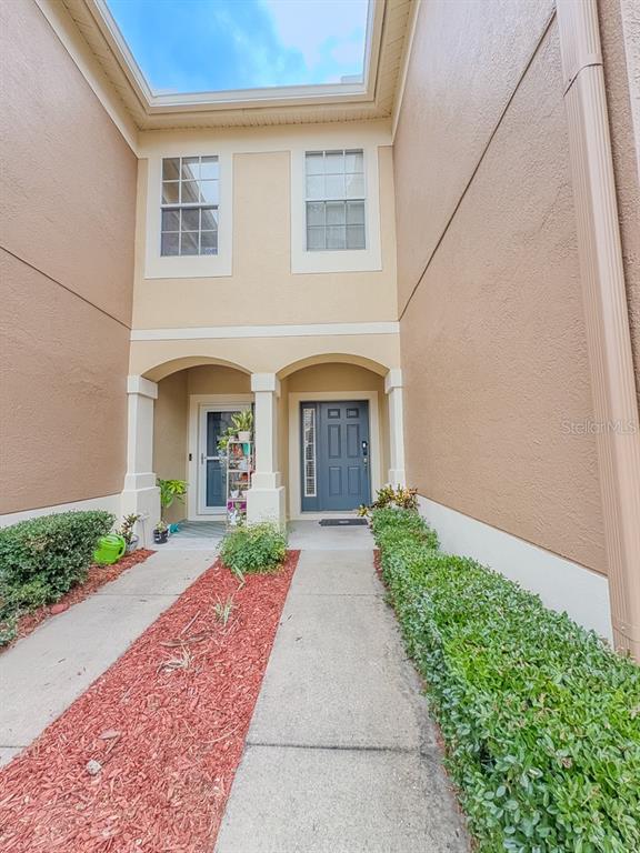 A two-story townhouse exterior features a concrete walkway, red mulch, and two front entry doors — 8505 SANDY BEACH STREET, TAMPA, FL