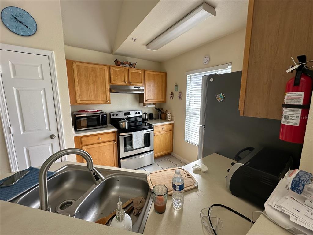 A kitchen features light wood cabinets, stainless steel appliances, a double sink, and a fire extinguisher — 9005 LEE VISTA BOULEVARD UNIT 1805, ORLANDO, FL
