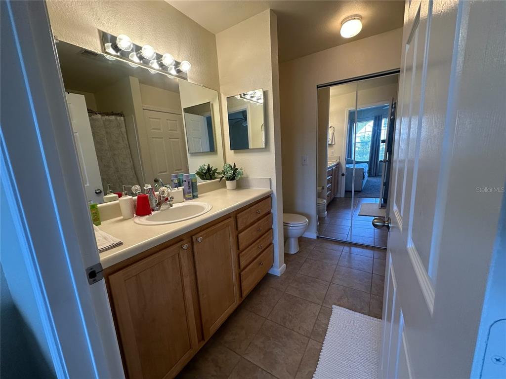 A bathroom features a wooden vanity, a large mirror, and a tiled floor — 9005 LEE VISTA BOULEVARD UNIT 1805, ORLANDO, FL