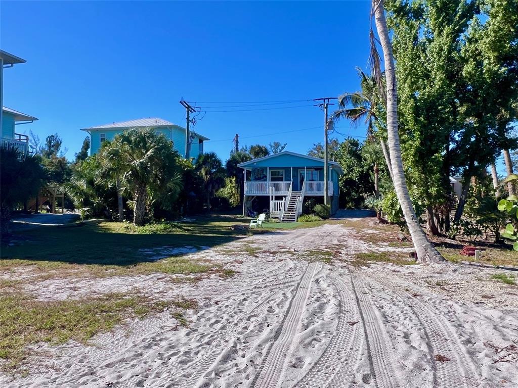 A sandy driveway leads to a raised blue house surrounded by palm trees and vegetation — 8142 LITTLE GASPARILLA ISLAND, PLACIDA, FL