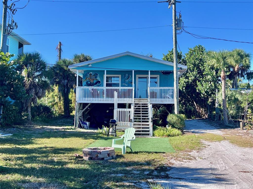 A turquoise elevated house features a front porch, stairs, and a brick fire pit below — 8142 LITTLE GASPARILLA ISLAND, PLACIDA, FL