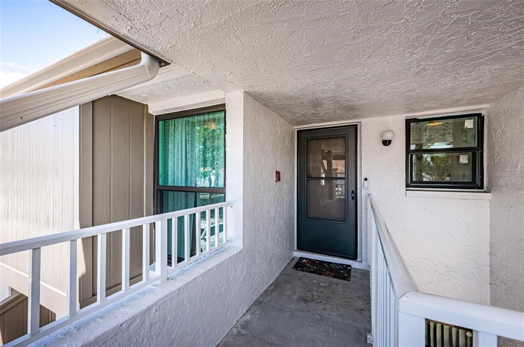 An exterior view of a covered balcony entrance with a dark door and white railings — 2117 LAKEWOOD CLUB DRIVE S UNIT 7K, ST PETERSBURG, FL