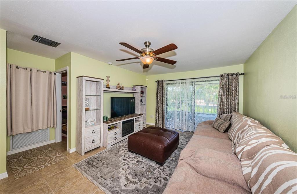 A living room features a brown leather ottoman, a patterned rug, and a media console — 2117 LAKEWOOD CLUB DRIVE S UNIT 7K, ST PETERSBURG, FL
