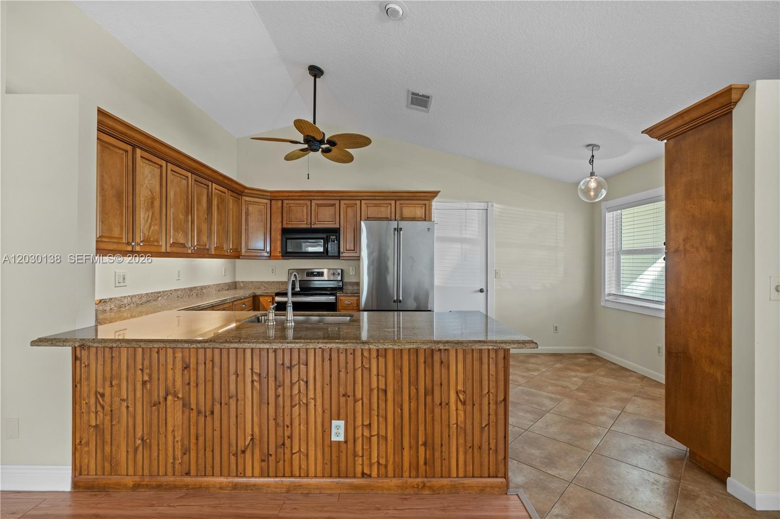 A kitchen features wood cabinets, granite countertops, a breakfast bar, and tile flooring — 132 Wandering Trl, Jupiter FL 33458, JUPITER, FL