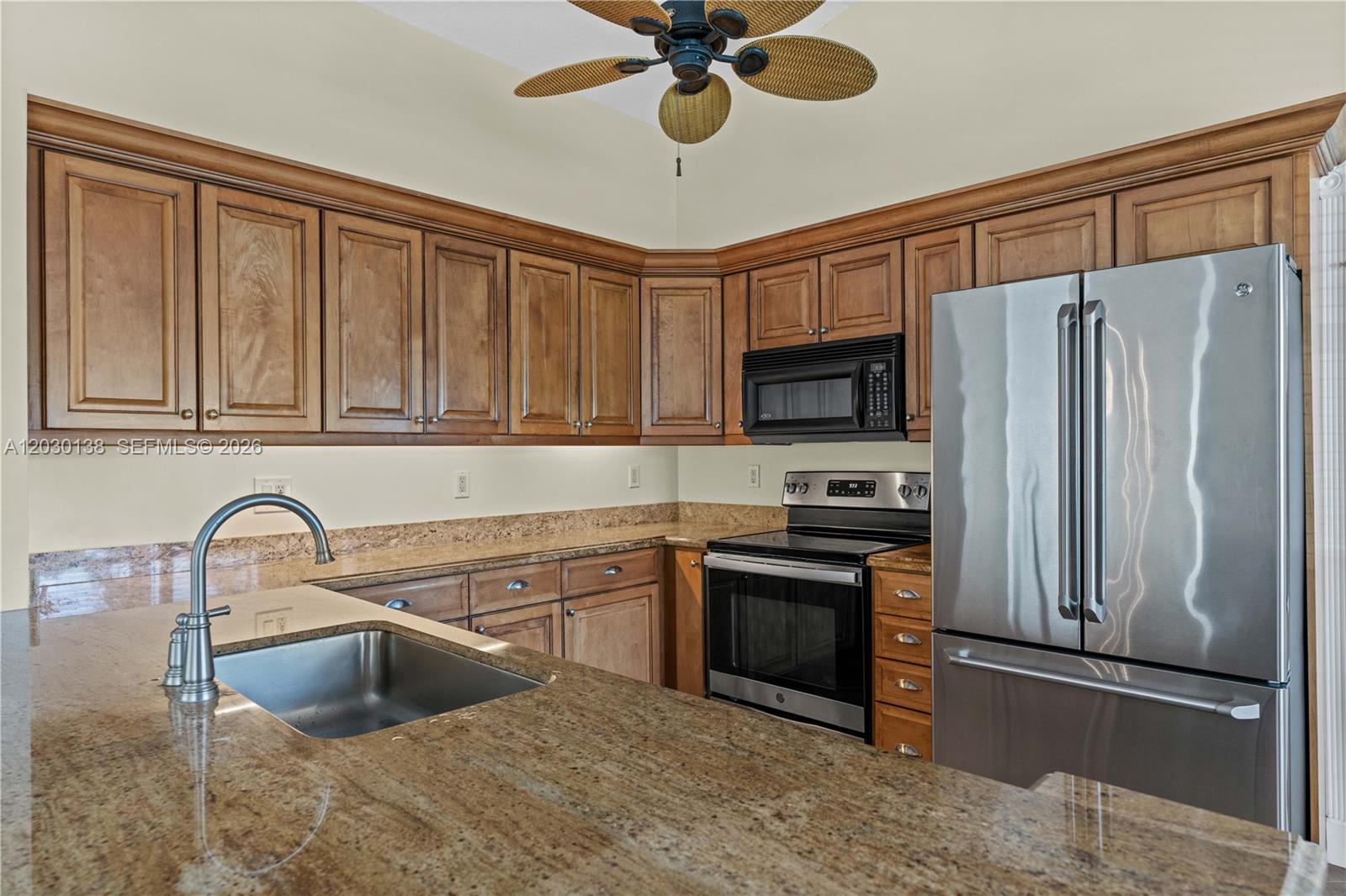 A kitchen features wood cabinets, granite countertops, stainless steel appliances, and a ceiling fan — 132 Wandering Trl, Jupiter FL 33458, JUPITER, FL