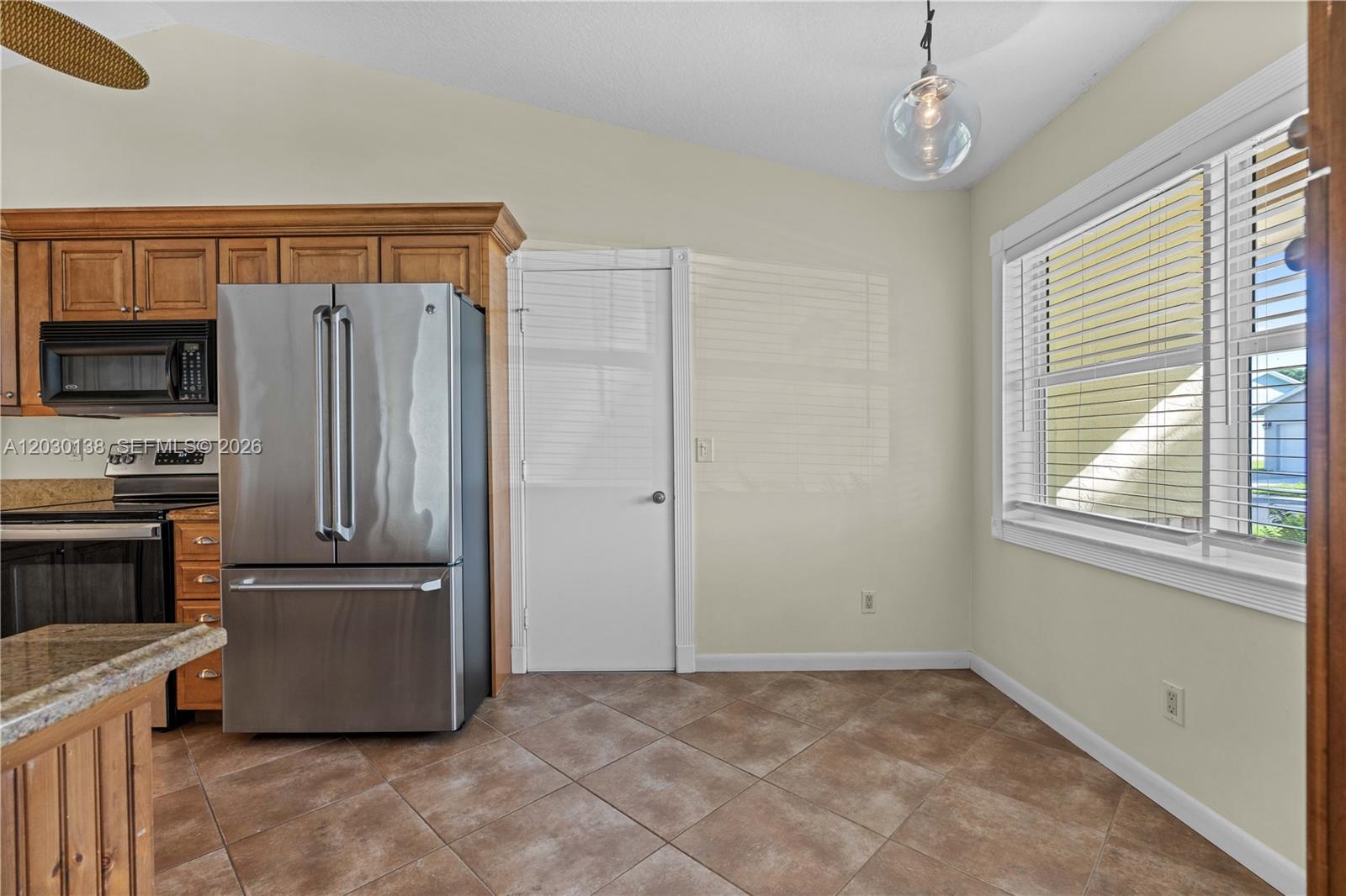 A kitchen features a stainless steel refrigerator, wooden cabinets, tile flooring, and a window — 132 Wandering Trl, Jupiter FL 33458, JUPITER, FL
