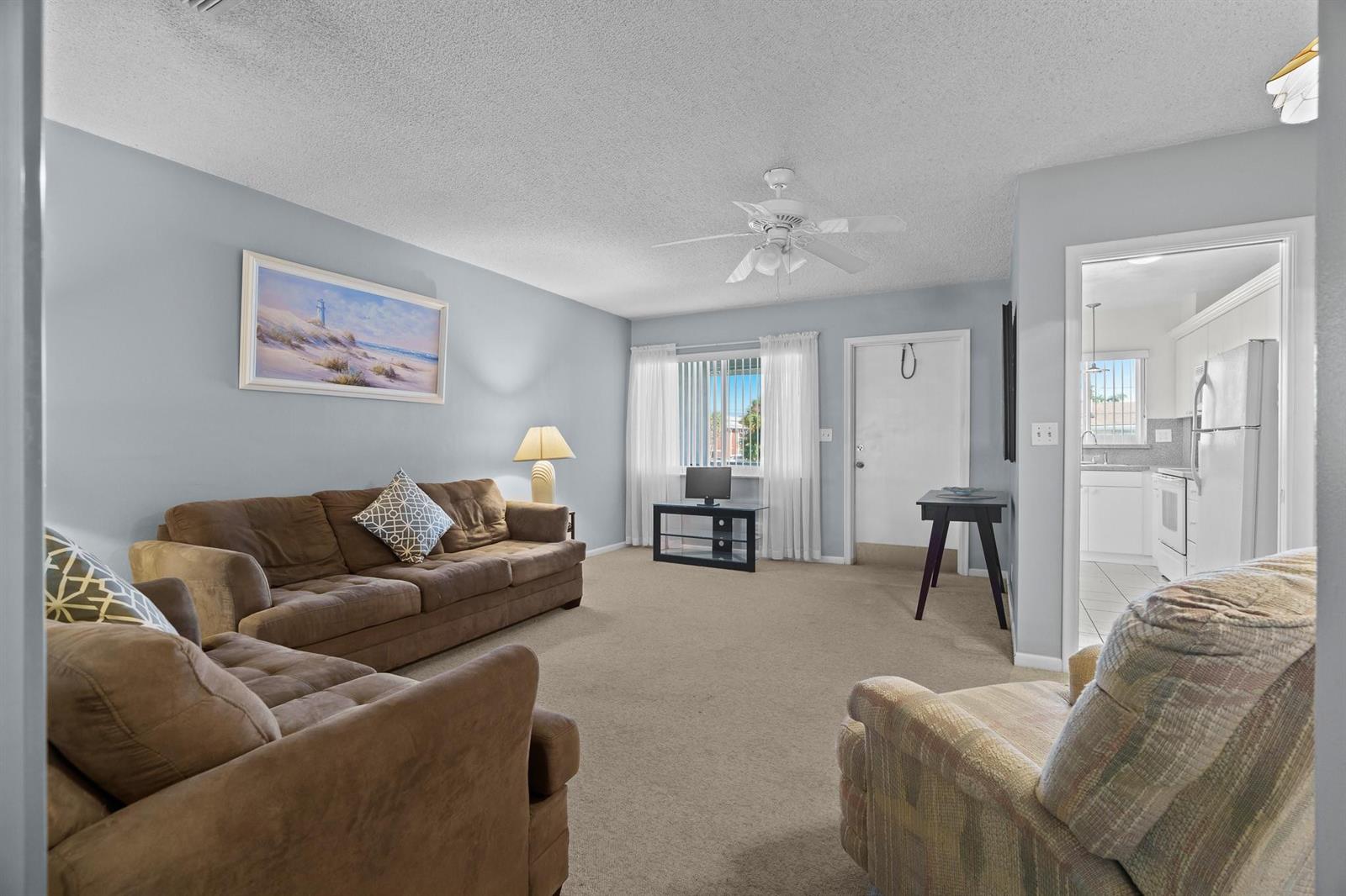 A living room with light blue walls, beige carpet, brown furniture, and a ceiling fan — 2100 NE 38th Street # 243, Lighthouse Point FL 33064, LIGHTHOUSE POINT, FL