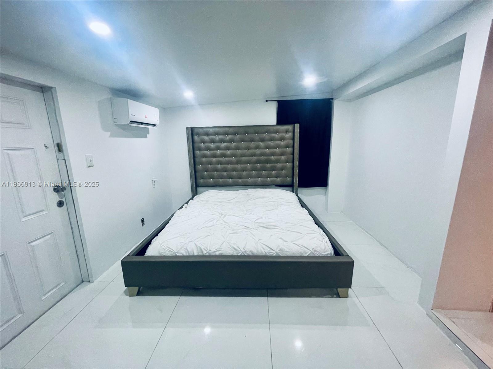 A bedroom features a tufted gray bed frame, white tile flooring, and a wall-mounted air conditioner — 2751 NW 99th St, Miami FL 33147, MIAMI, FL