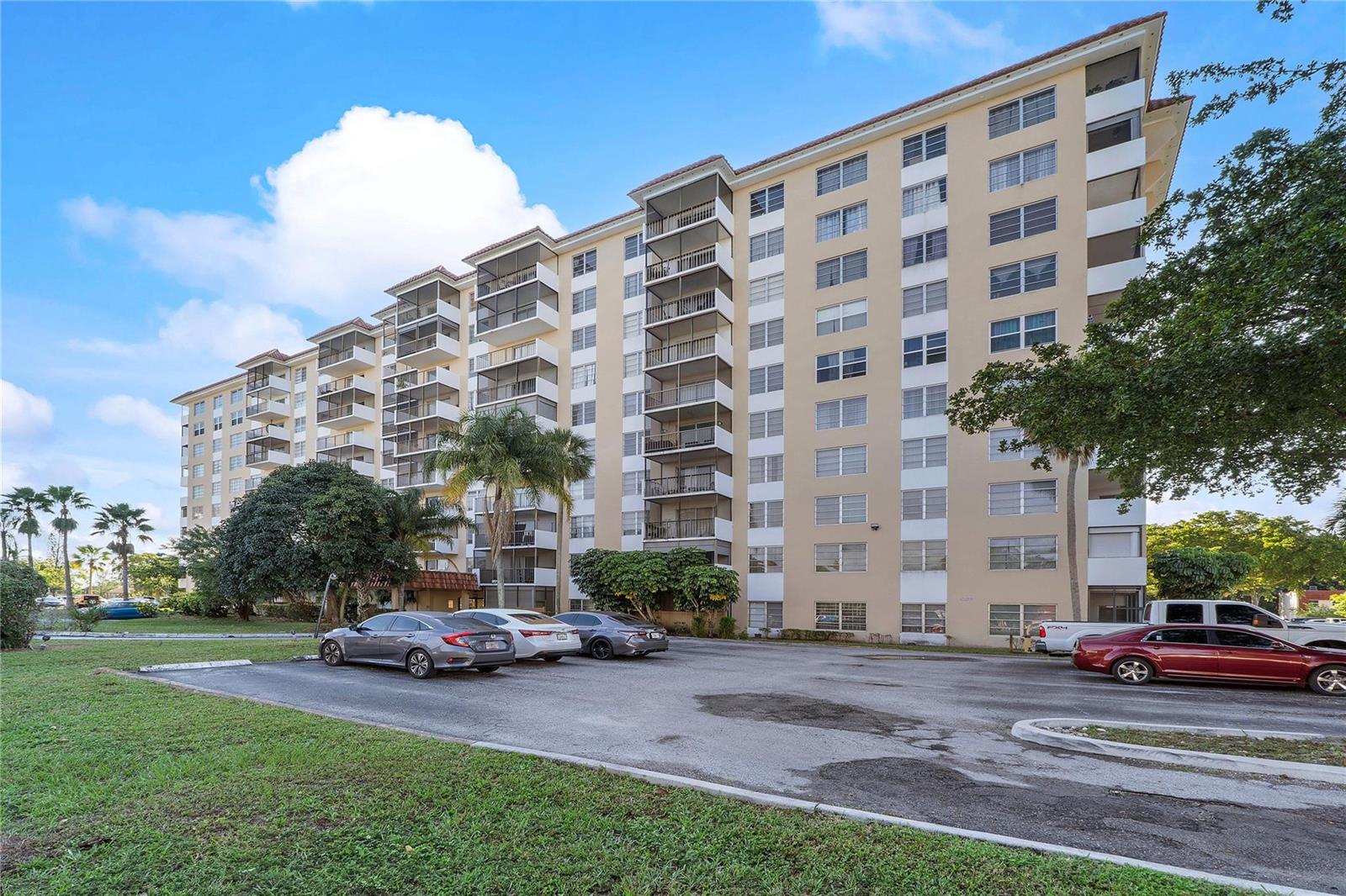 A multi-story apartment building with balconies stands behind a paved parking lot — 4174 Inverrary Drive # 1002, Lauderhill FL 33319, LAUDERHILL, FL