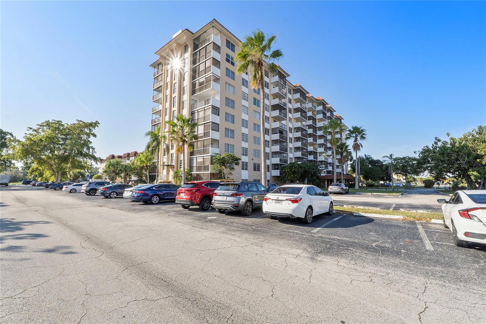 A multi-story apartment building stands behind a parking lot filled with various parked cars — 4174 Inverrary Drive # 1002, Lauderhill FL 33319, LAUDERHILL, FL