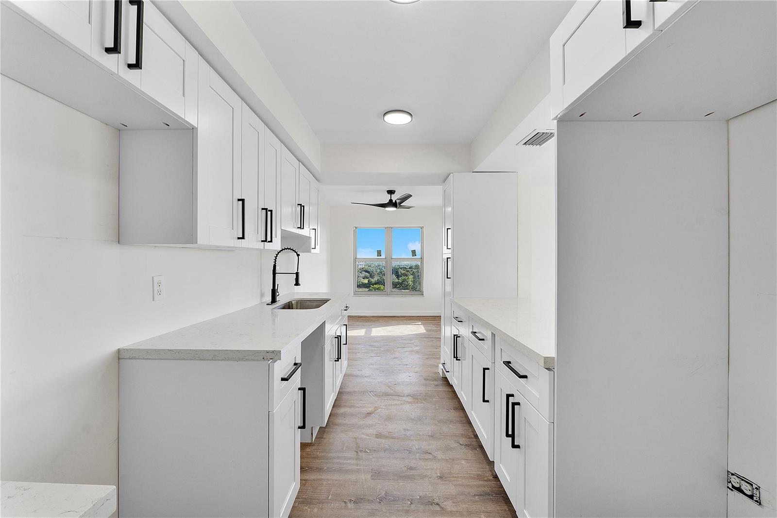 A galley kitchen features white cabinets, quartz countertops, black hardware, and a view of trees — 4174 Inverrary Drive # 1002, Lauderhill FL 33319, LAUDERHILL, FL