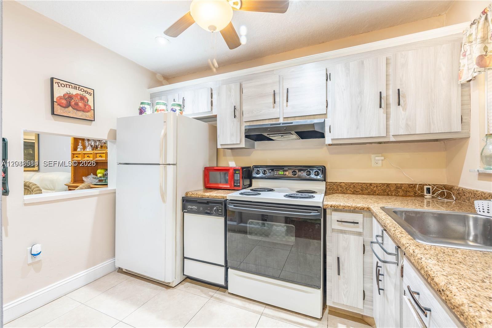 A kitchen features light wood-grain cabinets, granite countertops, white appliances, and a ceiling fan — 2811 N Pine Island Rd # 309, Sunrise FL 33322, SUNRISE, FL