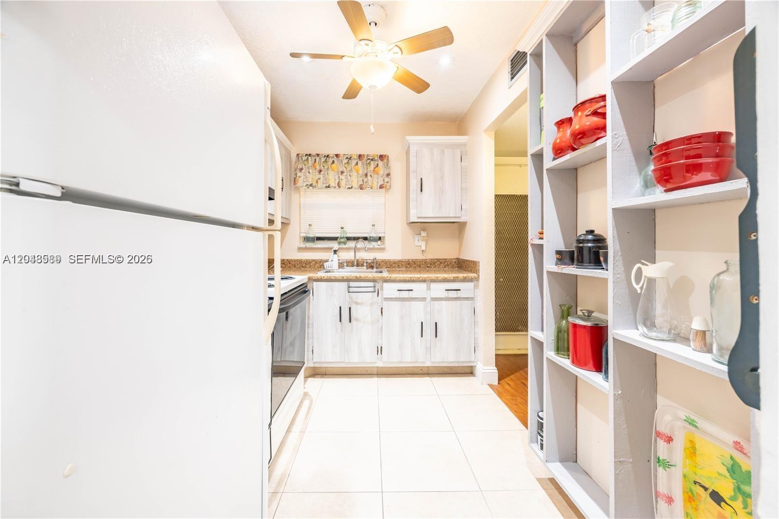 A galley kitchen features white cabinets, light countertops, tile flooring, and open shelving — 2811 N Pine Island Rd # 309, Sunrise FL 33322, SUNRISE, FL