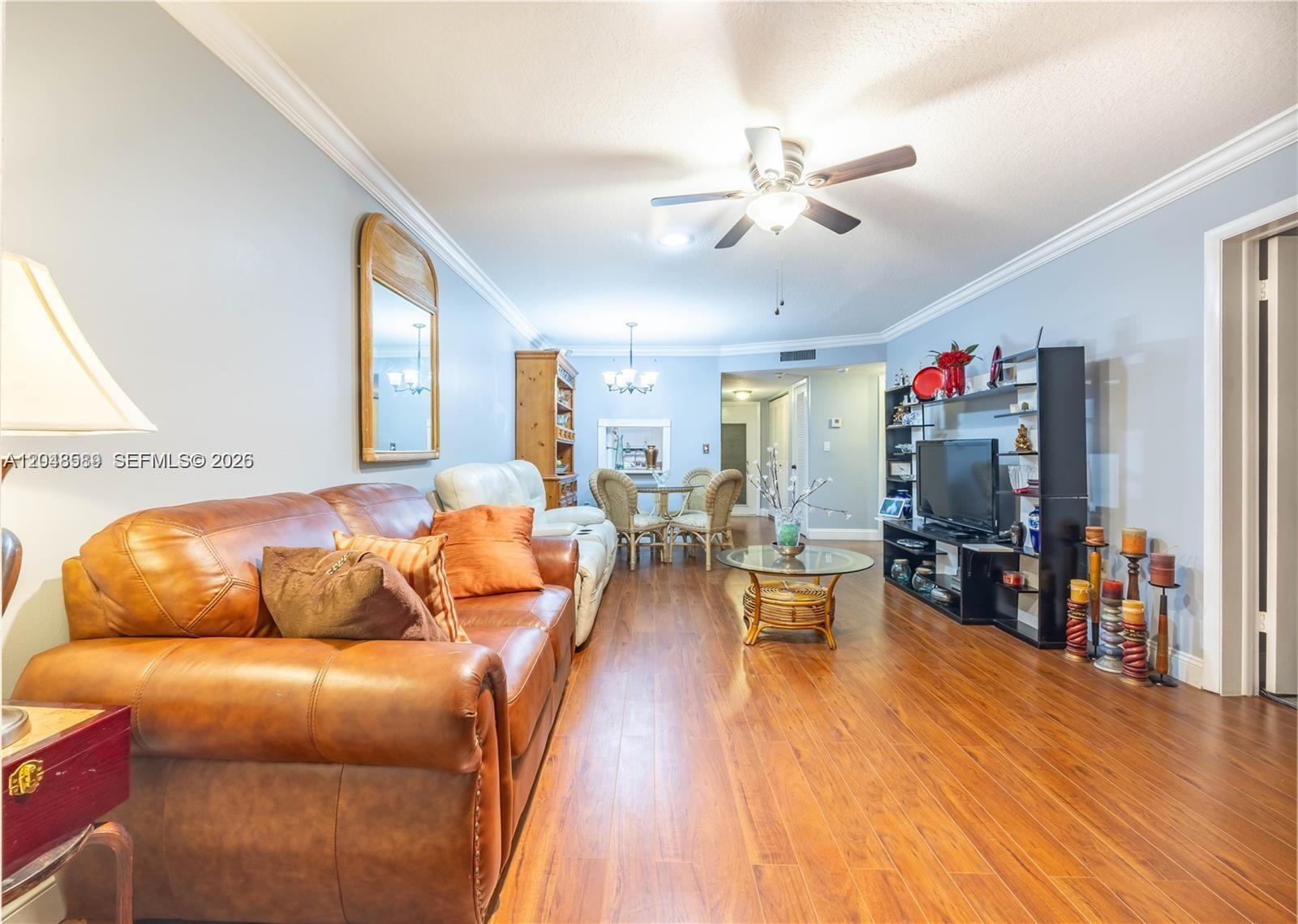 A living room features a leather sofa, wood flooring, a ceiling fan, and shelving — 2811 N Pine Island Rd # 309, Sunrise FL 33322, SUNRISE, FL