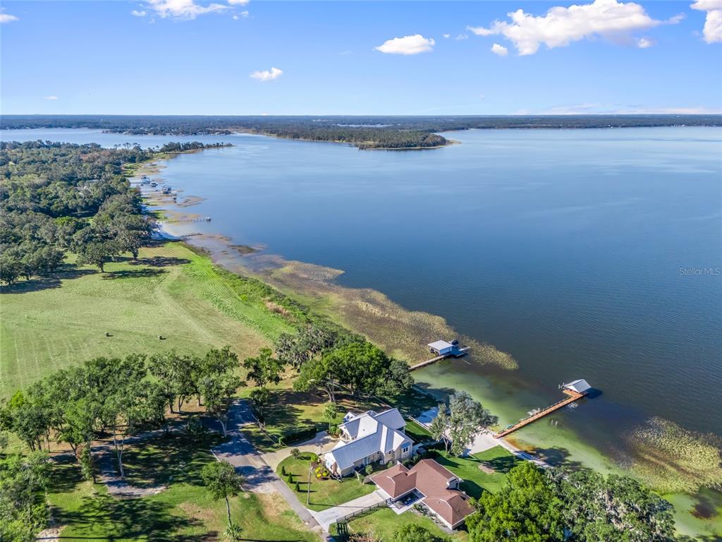 A multi-story yellow house with a balcony sits above a terraced lawn and sandy beach — 12943 SE SUNSET HARBOR ROAD, WEIRSDALE, FL
