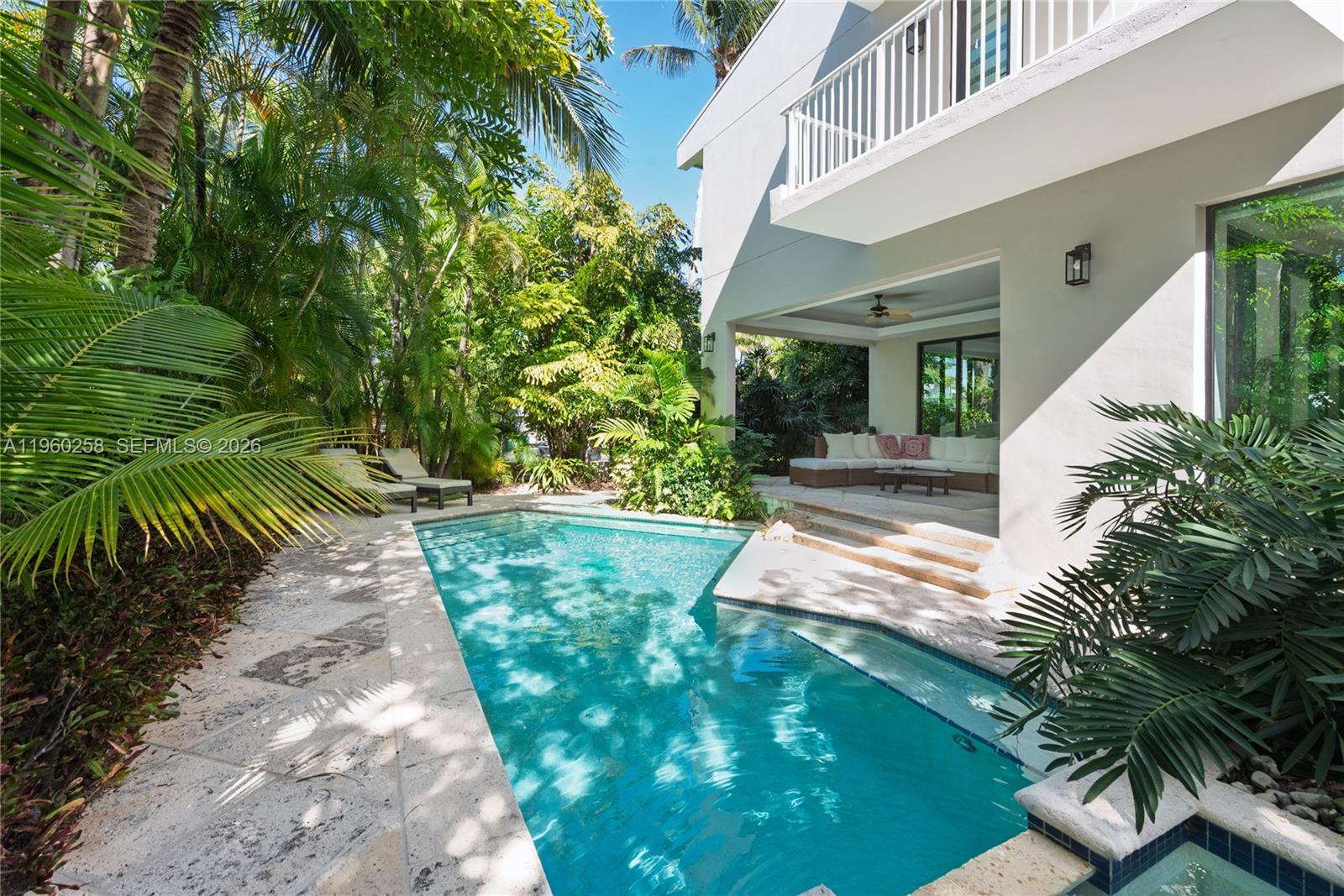 A swimming pool sits beside a modern house with a covered patio and lush landscaping — 650 Curtiswood Dr, Key Biscayne FL 33149, KEY BISCAYNE, FL