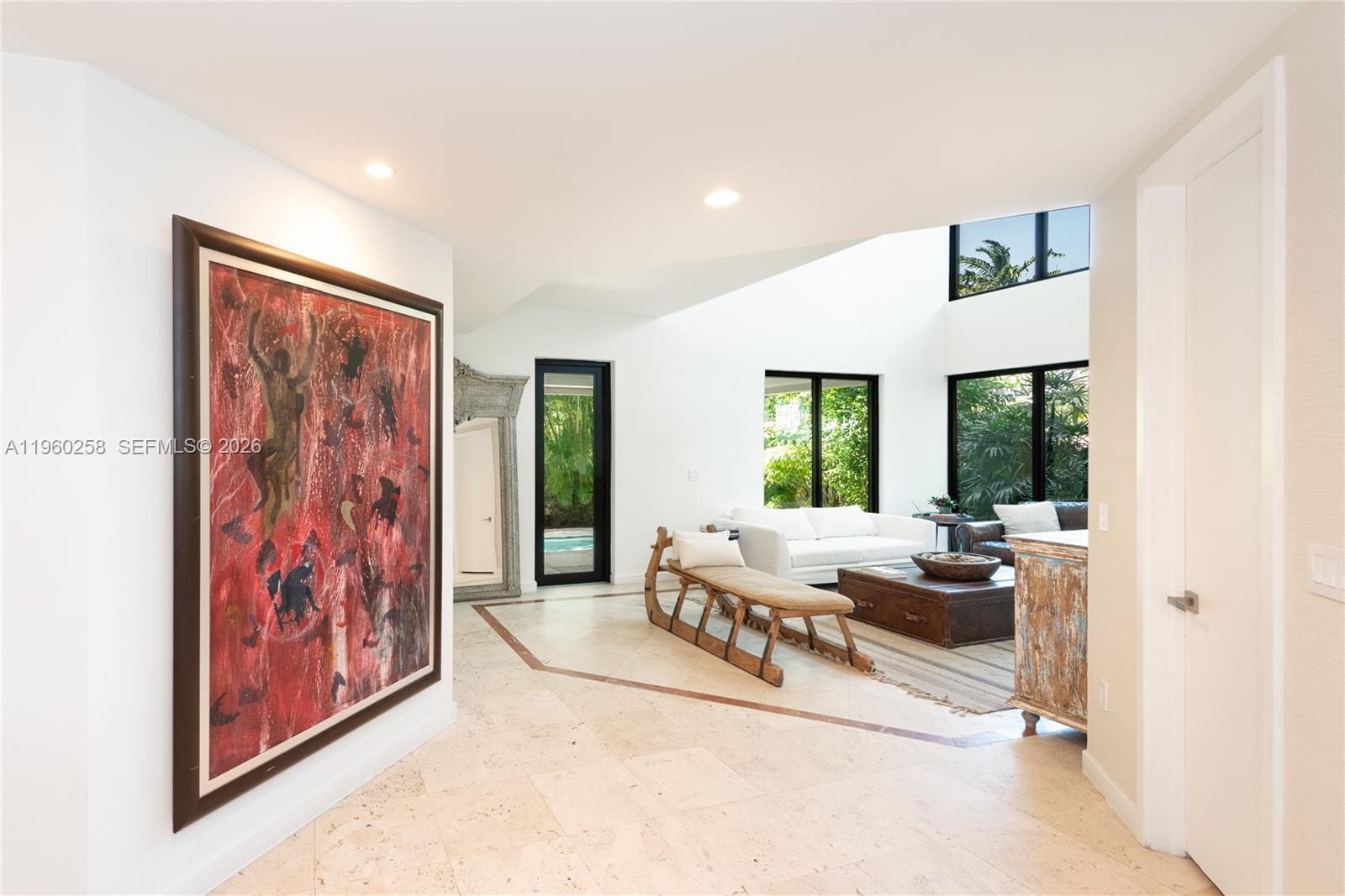 A bright living room features a large red painting, stone floors, and floor-to-ceiling windows — 650 Curtiswood Dr, Key Biscayne FL 33149, KEY BISCAYNE, FL