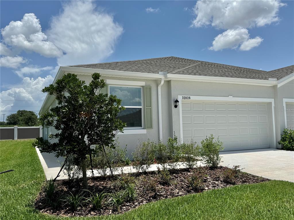 A single-story house exterior features a beige stucco facade, a garage, and a landscaped yard — 32828 RUSTIC RISE ROAD, SAN ANTONIO, FL