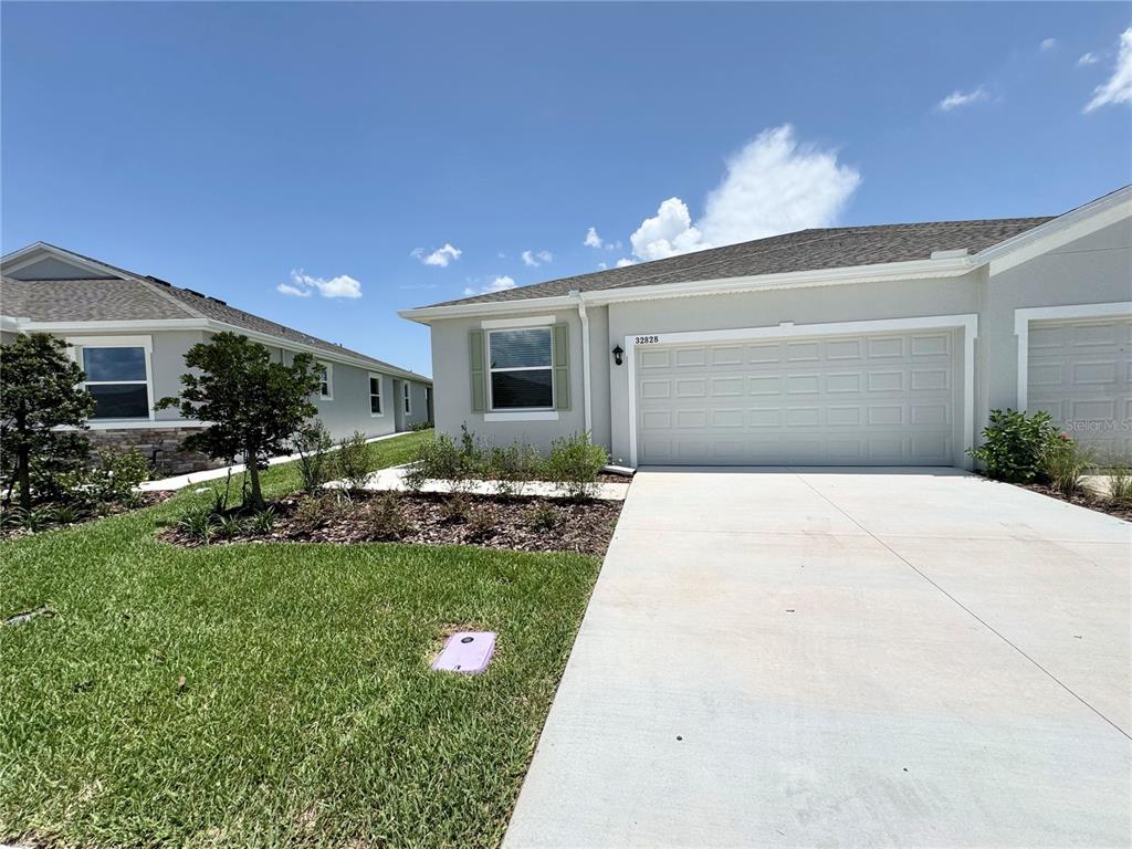 A light-colored single-story house features a two-car garage and a landscaped front yard — 32828 RUSTIC RISE ROAD, SAN ANTONIO, FL