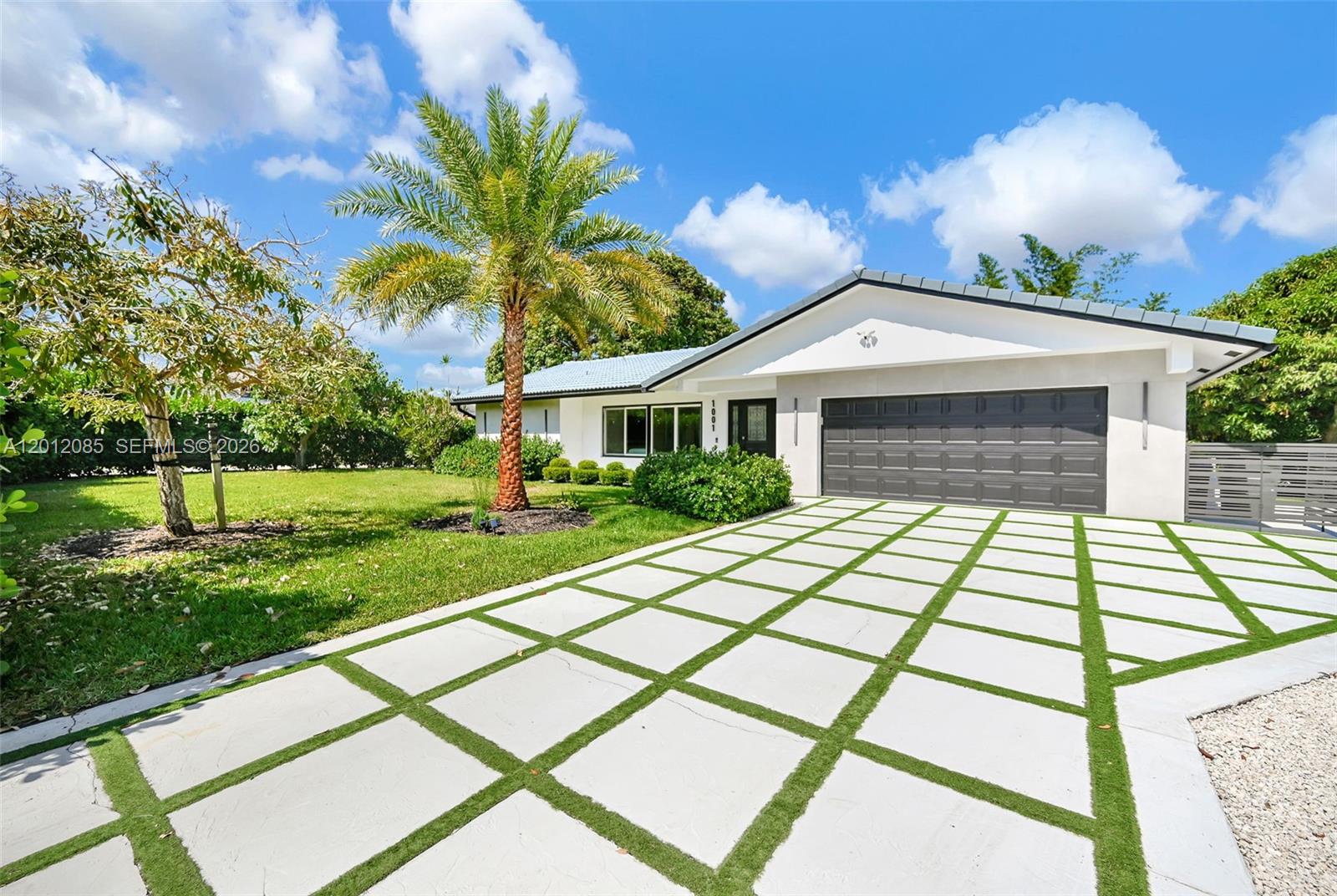 A single-story house features a white exterior, a dark garage door, and a grid-patterned driveway — 1001 NW 4th Ct, Boca Raton FL 33432, BOCA RATON, FL