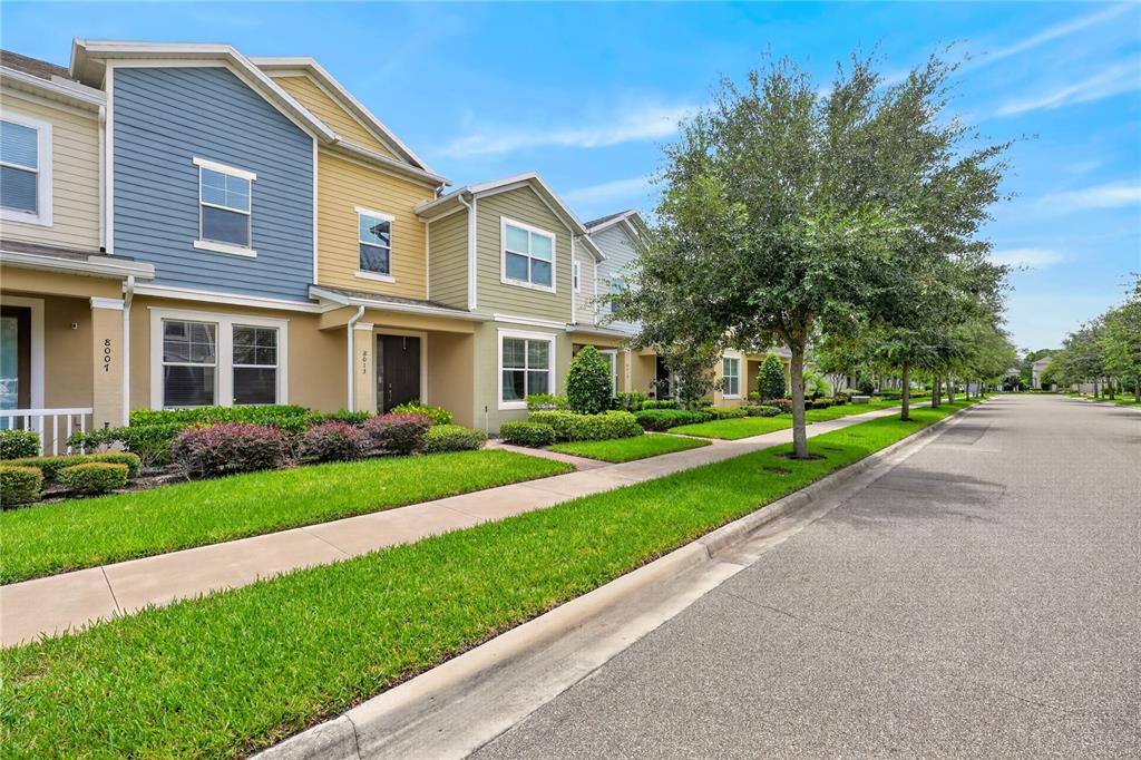 A row of colorful multi-story townhouses sits along a sidewalk and paved street — 8013 BASILICA LANE, WINTER GARDEN, FL