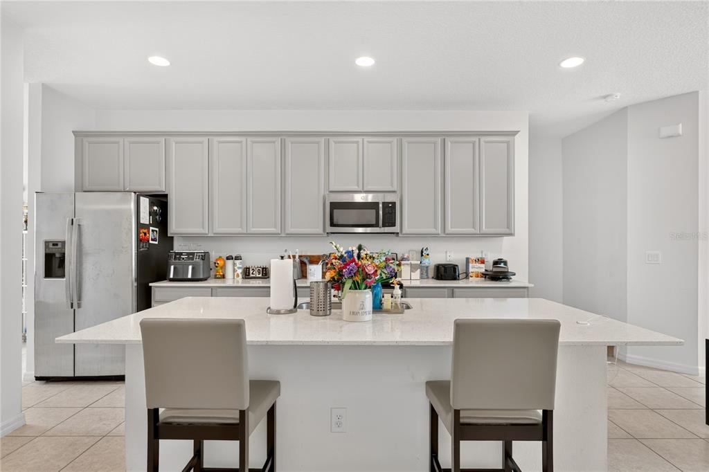 A kitchen features gray cabinets, stainless steel appliances, a white quartz island, and two chairs — 8013 BASILICA LANE, WINTER GARDEN, FL