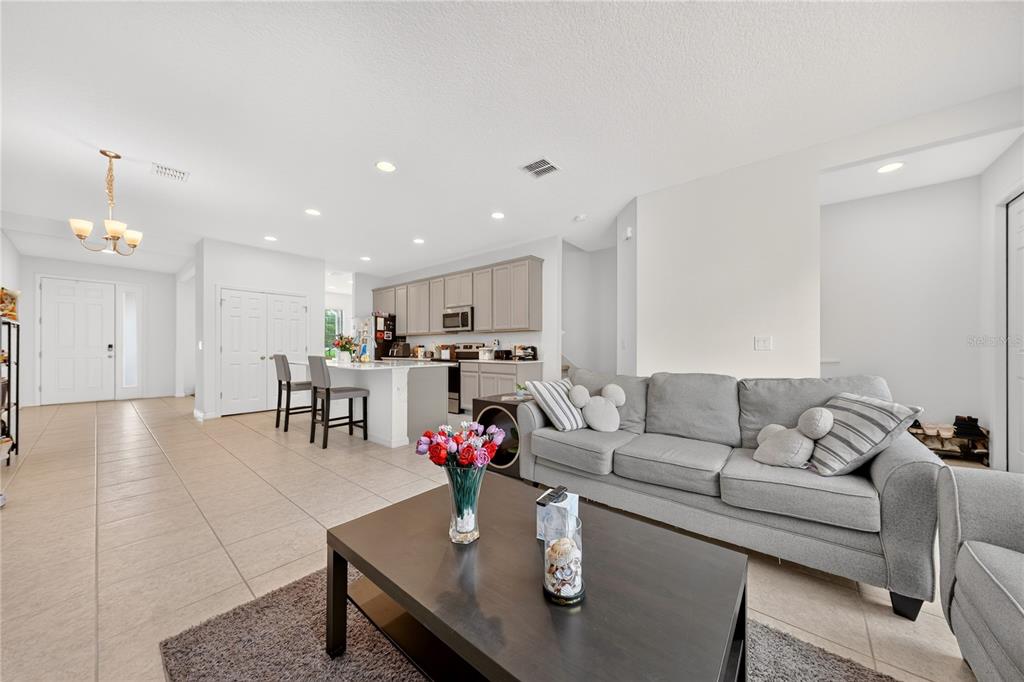 An open-concept living room and kitchen featuring tile flooring, a gray sofa, and light cabinetry — 8013 BASILICA LANE, WINTER GARDEN, FL