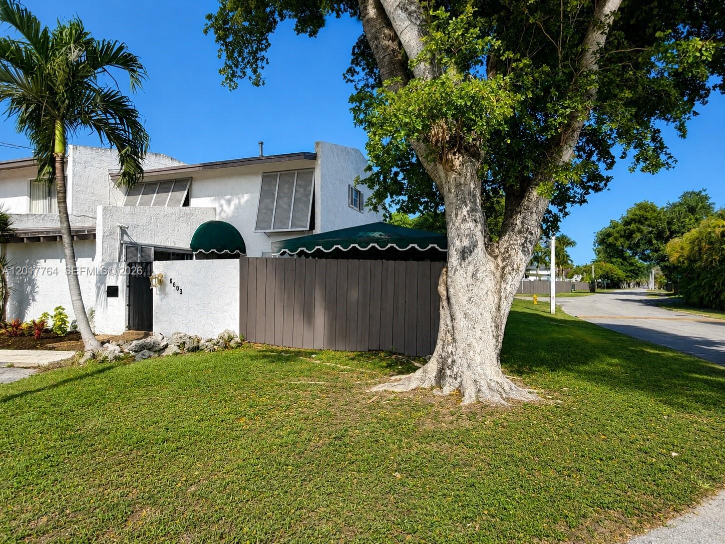 A white two-story house features a wooden privacy fence, green awnings, and a large tree — 6603 SW 112th Pl, Miami FL 33173, MIAMI, FL