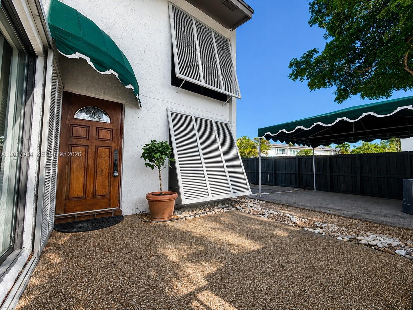 A white exterior wall features a wooden door, green awnings, and white louvered shutters — 6603 SW 112th Pl, Miami FL 33173, MIAMI, FL
