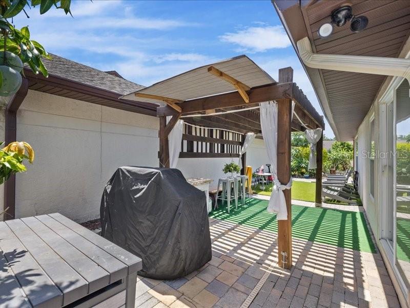 A backyard patio features a wooden pergola with white curtains over a paved floor — 10903 LANDON LANE, TAMPA, FL