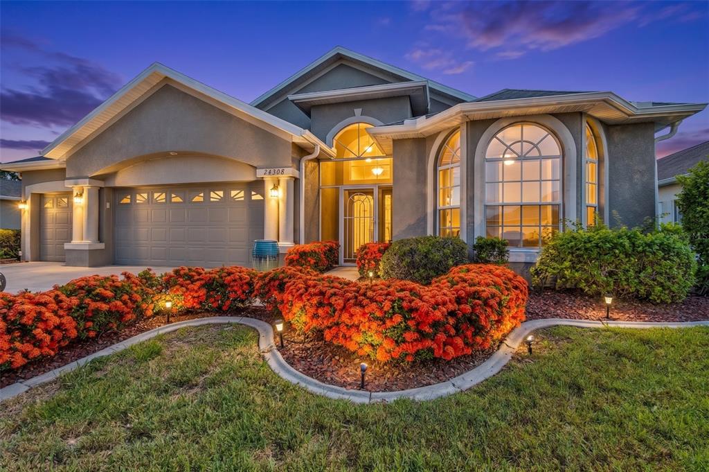 A single-story house with a gray stucco exterior, a two-car garage, and orange flowering shrubs — 24308 BUCKINGHAM WAY, PUNTA GORDA, FL