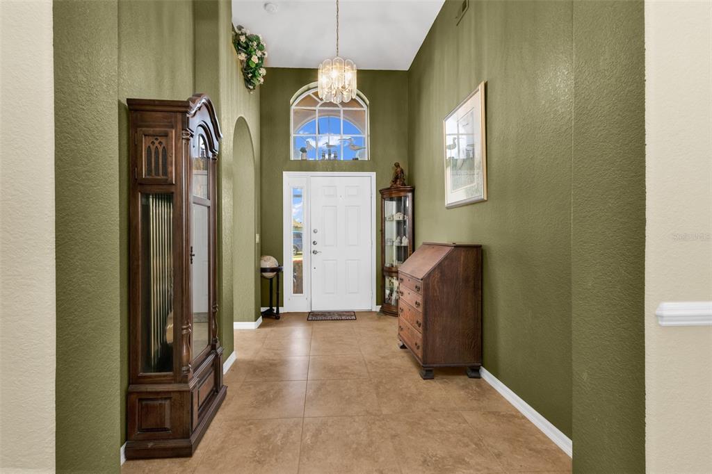 An entryway features olive green walls, tile flooring, a grandfather clock, and a white door — 24308 BUCKINGHAM WAY, PUNTA GORDA, FL