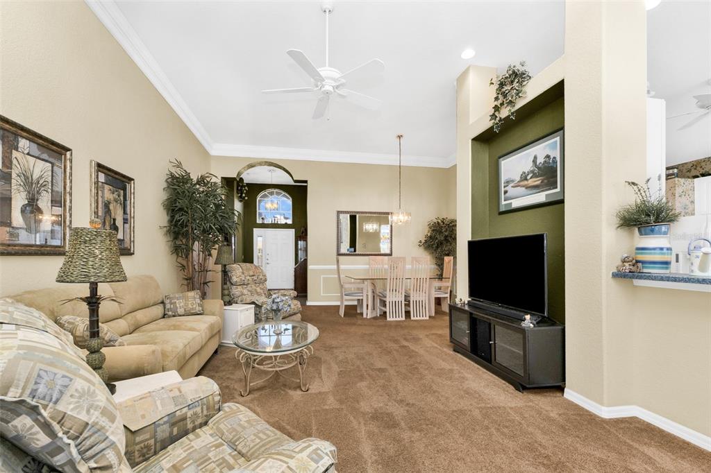A living room with beige carpet, a tan sofa, and a television on a black stand — 24308 BUCKINGHAM WAY, PUNTA GORDA, FL